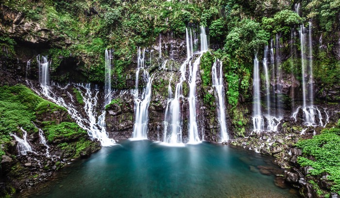 Multiple waterfalls cascade down mossy rocks into a turquoise pool