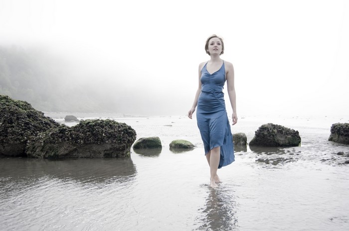 Woman in blue dress walking on a foggy beach with stones