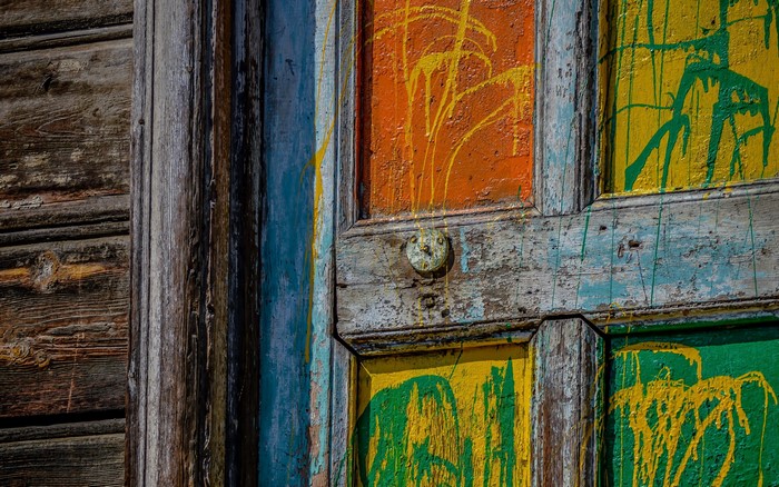 Close-up of a weathered wooden door with colorful paint splatters