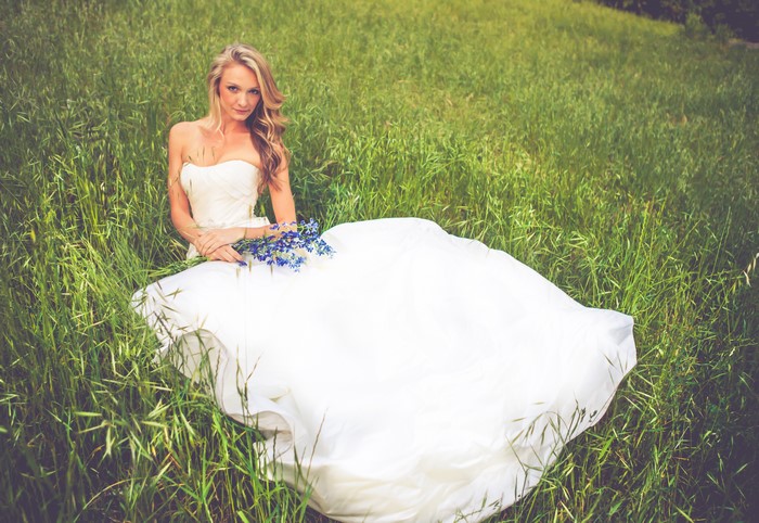 Bride in a white dress sitting in grass with flowers