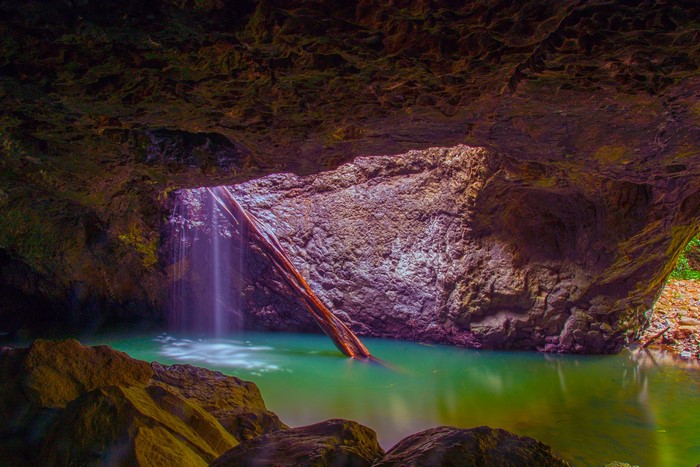 Cave with waterfall and log in green water