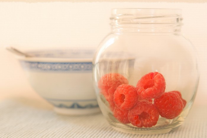 Raspberries in a glass jar next to a bowl