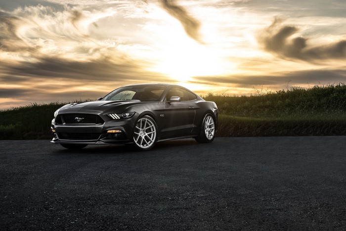 Black Ford Mustang GT on asphalt road at sunset