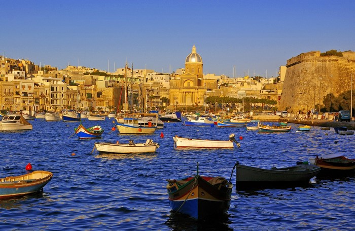 Boats in a harbor with buildings and a church in Malta
