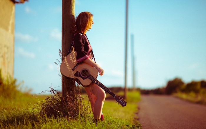 Girl with guitar leaning on pole by road