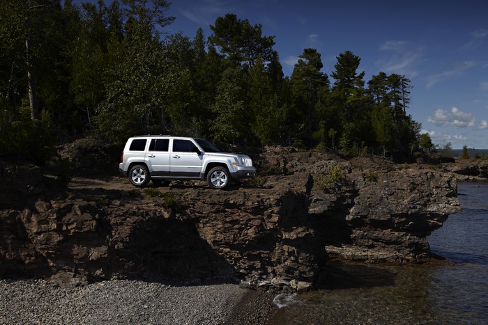 White Jeep Patriot on a rocky coast with forests