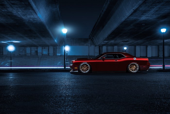 Red Dodge Challenger parked under bridge at night