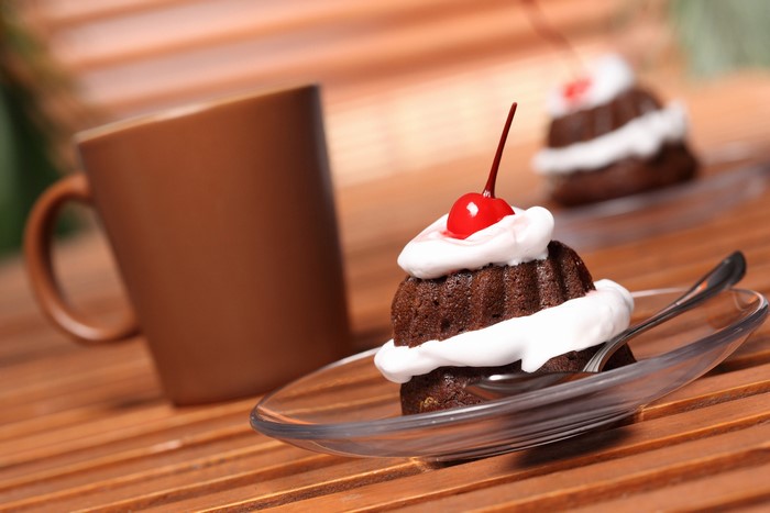 Chocolate cakes with whipped cream and cherries next to a mug