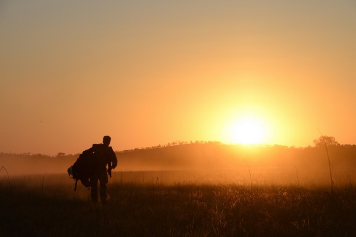 Soldier carrying gear at sunrise in a field
