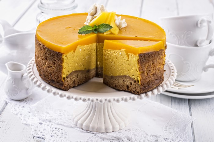 Mango cheesecake with a slice removed on a cake stand