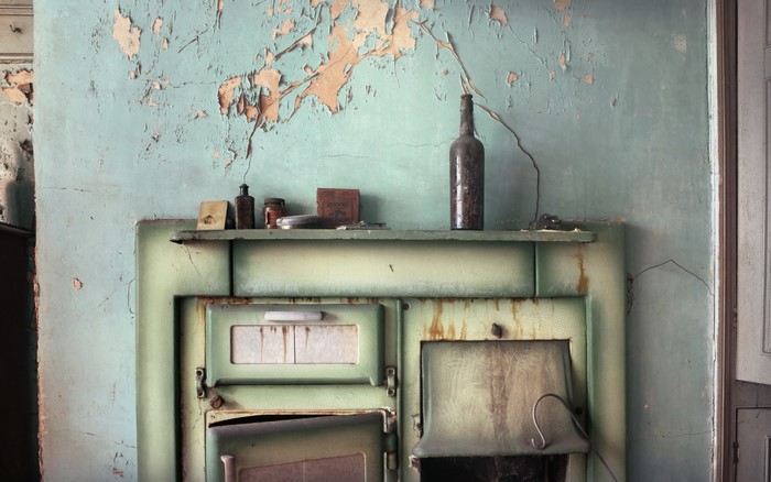 Old stove with peeling paint and bottles on shelf