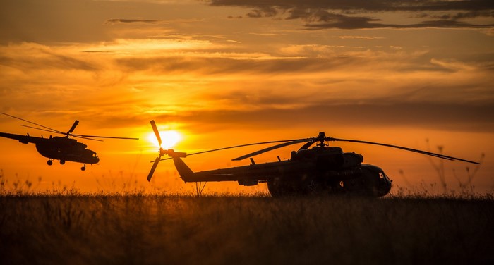 Two helicopters silhouetted against a sunset