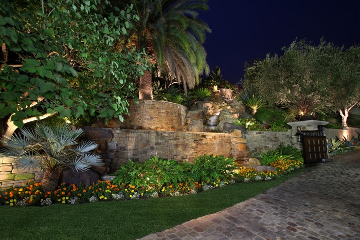 Illuminated garden with waterfall and palm trees at night