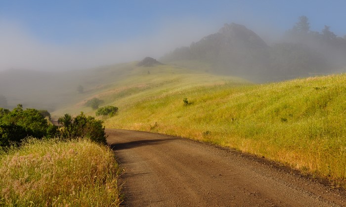Dirt road through foggy hills with mountains