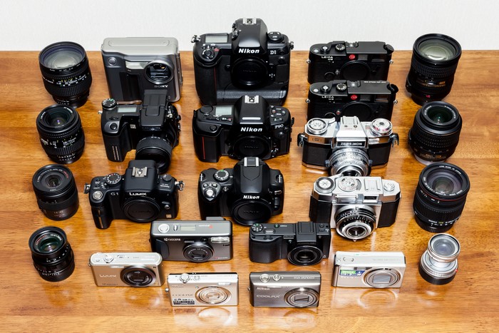 Many cameras and lenses on a wooden surface