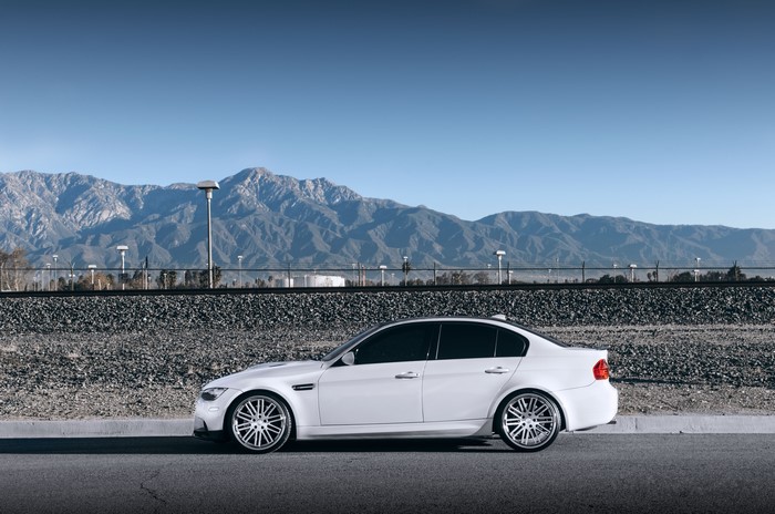 White BMW M3 E90 parked by railroad tracks with mountains
