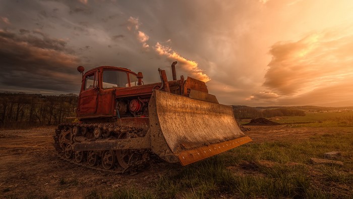 Red bulldozer in a field at sunset