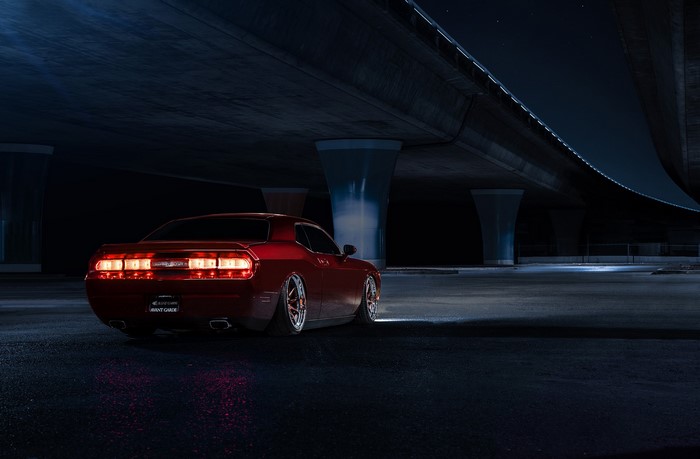 Red Dodge Challenger under a bridge at night