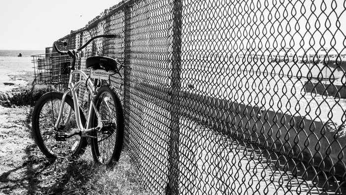 Bicycle leaning against a chain-link fence at the beach
