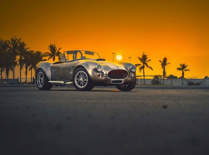 Classic AC Cobra convertible at sunset with palm trees