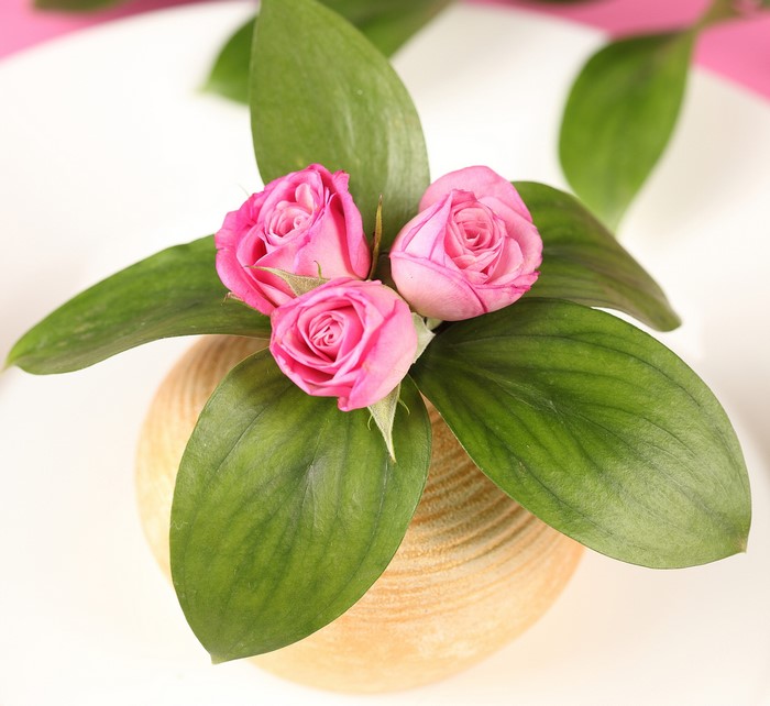 Three pink roses in a textured vase with green leaves