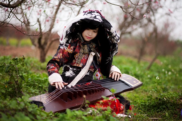 Girl playing a traditional Asian instrument outdoors