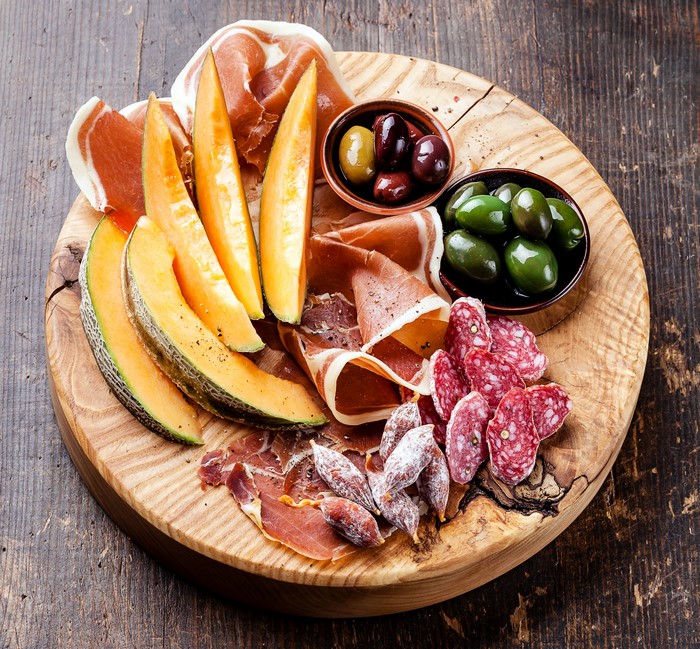 Charcuterie board with cured meats, melon, and olives