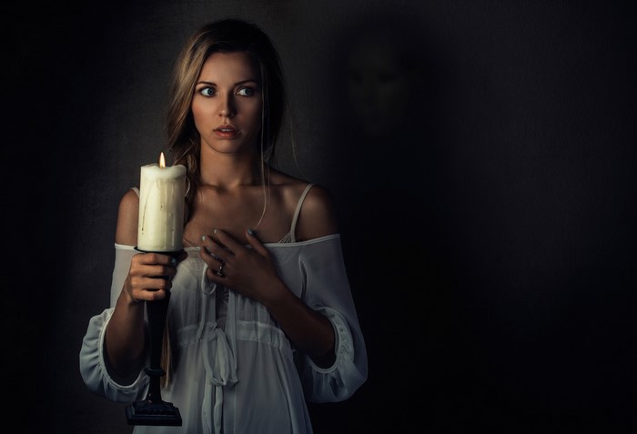 Woman holding a candle with a shadowy figure behind her