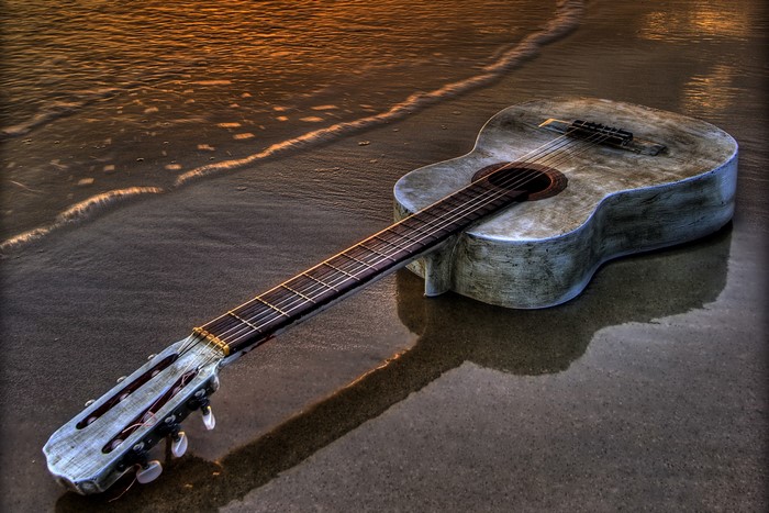 Acoustic guitar on a sandy beach with waves