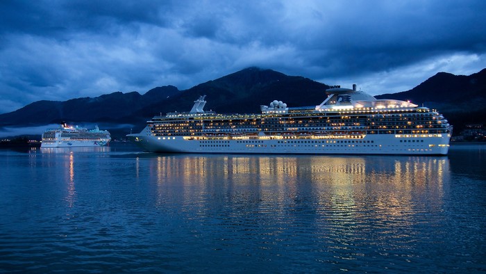 Two cruise ships at night with mountains in the background