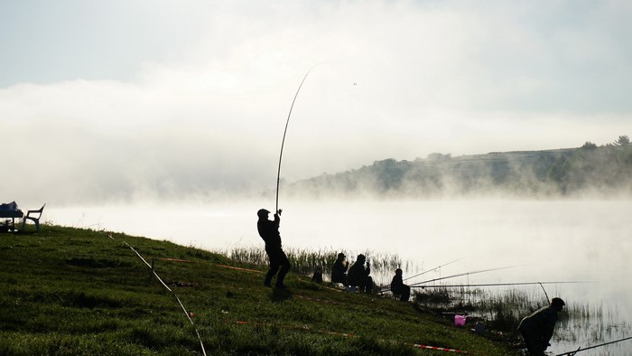 Fishermen on a foggy lake at sunrise