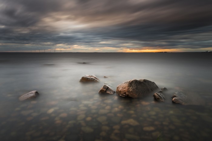 Long exposure of stones in water with wind turbines on horizon