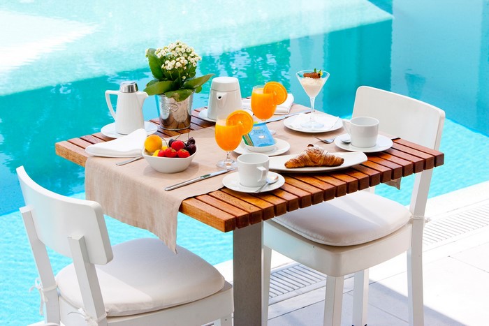 Breakfast table by the pool with fruit, croissants, and orange juice