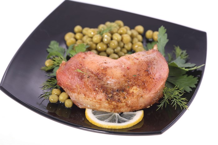 Roasted meat with peas, dill, and lemon on a black plate