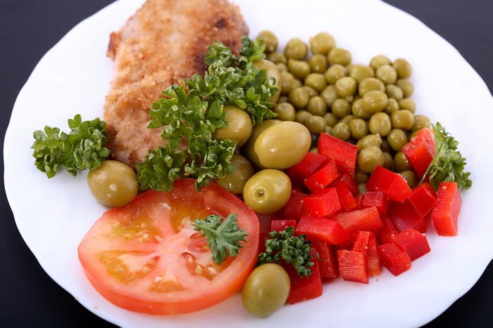 Breaded meat with peas, olives, tomatoes, and bell peppers on a plate