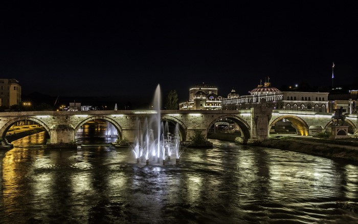 Stone bridge with fountains over river at night in Skopje, Macedonia