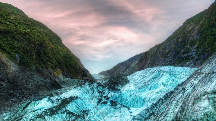 Glacier between green mountains under pink sky
