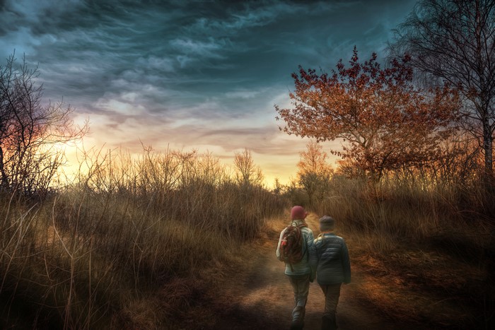 Two children walking on a trail under a stormy sky
