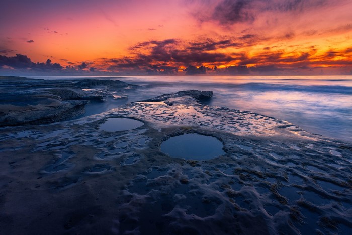 Sunset over the ocean with rocky shore and tide pools