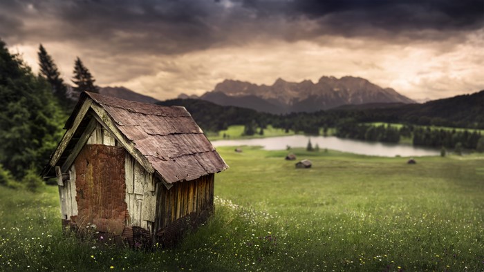 Old wooden cabin by a lake with mountains