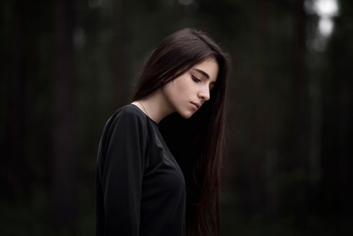 Brunette girl looking down in a dark forest