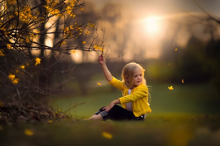 Young girl in yellow cardigan sitting in a field with yellow flowers
