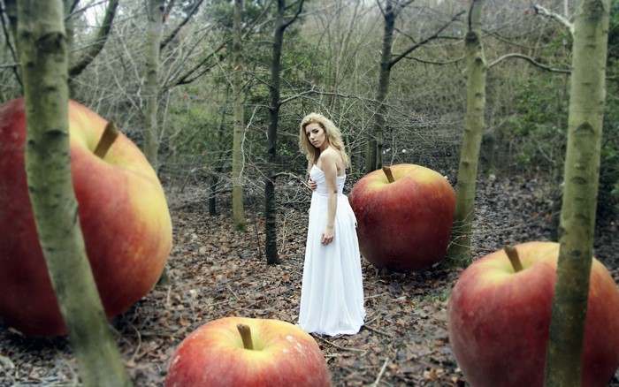Woman in white dress with giant apples in forest