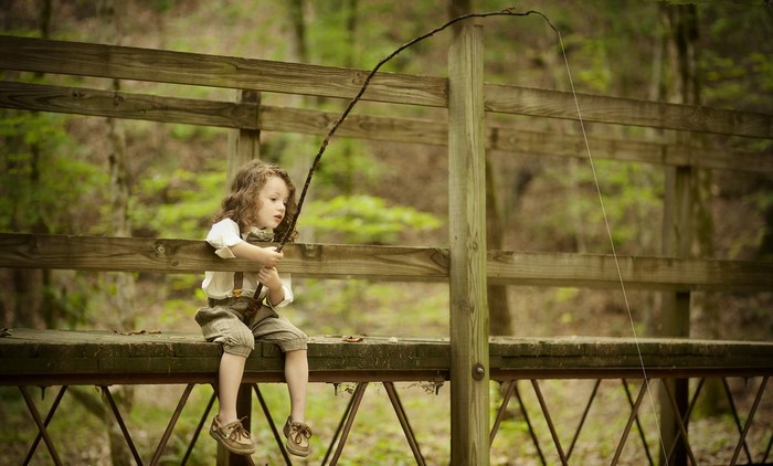 Young girl fishing with a stick on a wooden bridge