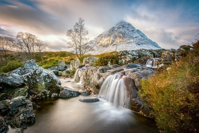 Waterfall flowing over rocks with snow-capped mountain in background