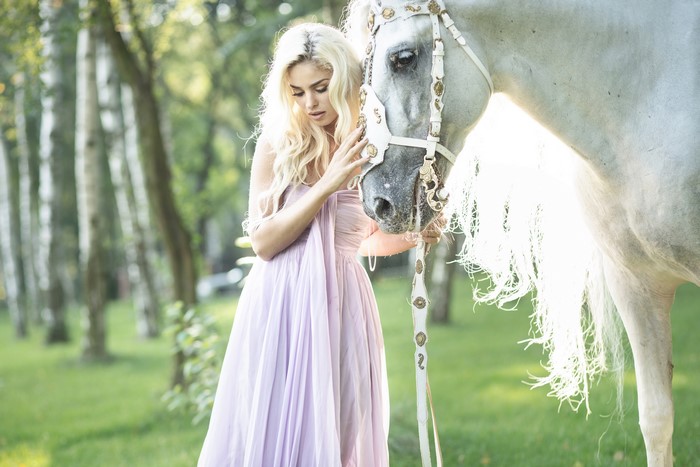 Blonde girl with white horse in park