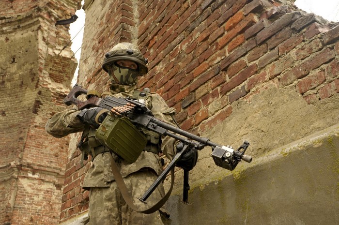 Ukrainian soldier with machine gun in front of brick wall