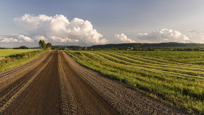 Dirt Road Through Agricultural Fields Under Cloudy Sky