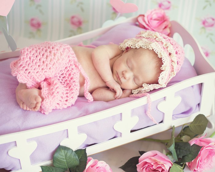Newborn baby sleeping in a crib with pink roses