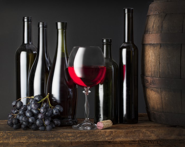Wine bottles, glass of red wine, grapes, and barrel